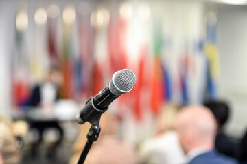 Detail shot with a microphone during a press conference. Audience in the background.
