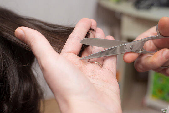 Mother's hands with scissors, trimming her son's hair at home. Soft focus close up. 