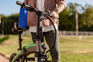 details of hipster stylish man in park listening to music on using electric bicycle
