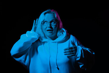 curious woman in glasses in a hoodie eavesdrops in blue light on a black background