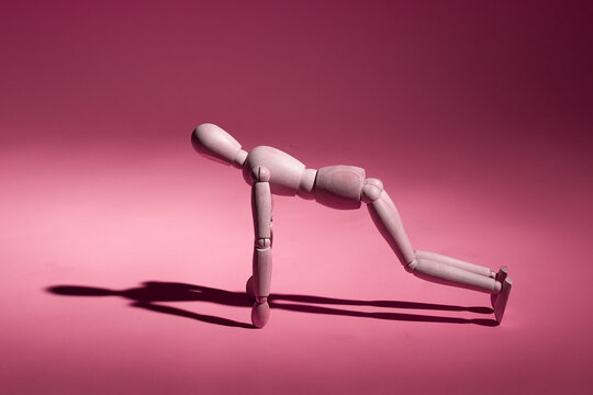 wooden mannequin doing push-ups from the floor on a pink background