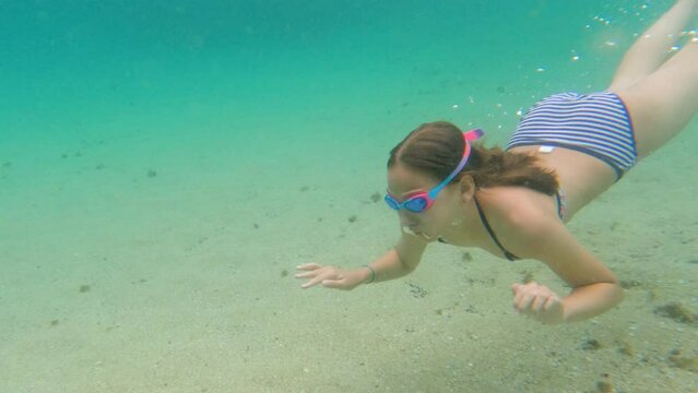 Child girl swimming underwater with swim goggles. Dives and swimming in the sea. Have fun on summer vacation. 4K slow motion.