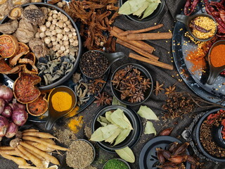 A view from the top of various spices and different colors laid on a table covered with brown cloth. Spices used in cooking include bael, turmeric powder, cloves, galingale, onions, dried chilies, etc