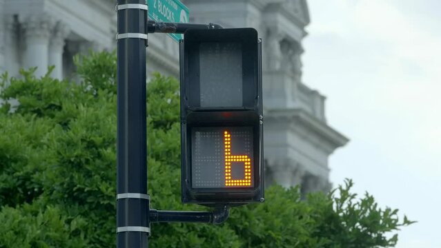 Modern LED street light walk signal counting down for pedestrian crosswalk  on corner to allow people on foot to traverse a busy intersection of roads with cars at a stop light