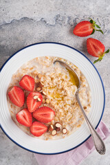 Oatmeal. Bowl of oatmeal porridge with strawberry, almond and milk on vintage light grey teal table. Top view in flat lay style. Natural ingredients. Hot and healthy breakfast and diet food.