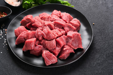 Raw chopped beef meat. Raw organic meat beef or lamb, spices, herbs on black plate on dark grey concrete background. Goulash.  Raw uncooked meat. Meat with blood. Top view with copy space.