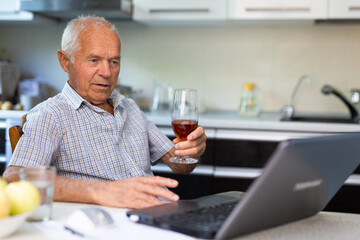 Fototapeta na wymiar Senior man with glass of brandy and laptop