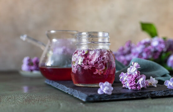 Preparation of syrup from the lilac flowers. Glass jar of homemade lilac syrup and branch of lilac flowers, stone background.