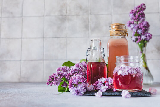 Preparation of syrup from the lilac flowers. Glass jar of homemade lilac syrup and branch of lilac flowers, stone background.