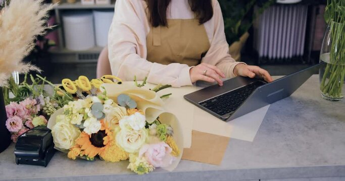 Close up. Young adult Caucasian woman small business owner working on laptop in store checking inventory. Florist worker, female botanist typing on keyboard computer.