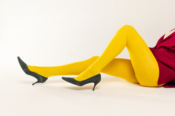 Cropped image of female legs in yellow bright tights and heels isolated over grey studio background