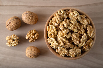 Bowl of walnuts and whole walnut kernels on wooden background,top view