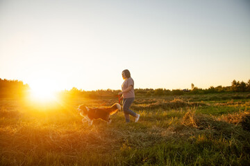 Fototapeta na wymiar Beautiful woman walking out her dog in sunset field
