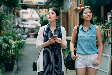 lost Asian traveling girls are using gps app on the phone for direction and looking around at an...