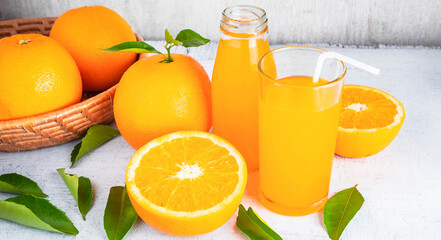 Fresh orange juice and orange fruit are in a basket on a white wooden background.