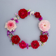 round frame of fresh roses and flowers on a gray background, top view