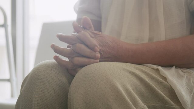 An Asian elderly woman sits anxiously holding her hand as she waits for a check-up at the hospital.