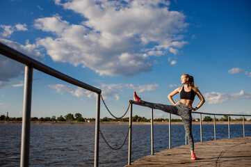 Slim fit woman doing stretching exercises on pier at sunny day