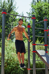 Obraz premium Shirtless man doing loop exercises outdoors in summer park.