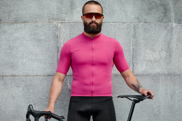 Cyclist in pink sportwear resting after an workout while standing against cement wall background...