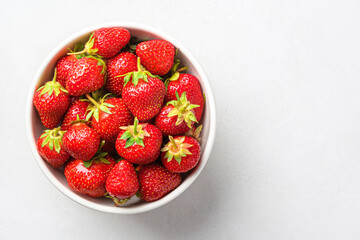 Fresh strawberries in a white bowl on a gray background. Top view, copy space.
