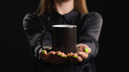 mockup of a black mug in female hands on a dark background