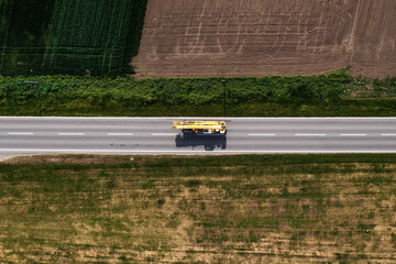 Fototapeta na wymiar Crane truck or boom-truck on the road through countryside landscape, aerial shot from drone pov