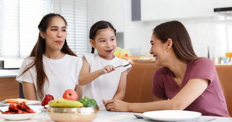 A cute little daughter is feeding her aunt's bread with her mother smiling