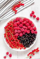 Fresh raspberry, red and black currant in a white plate. Top view.