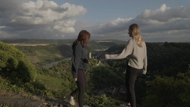 drone footage revealing two girls hugging of joy with the niederburg castle near kobern next to the moselle river in germany in the background