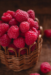 Fresh sweet raspberries in a wicker basket on a wooden background. Organic food and clean eating concept.