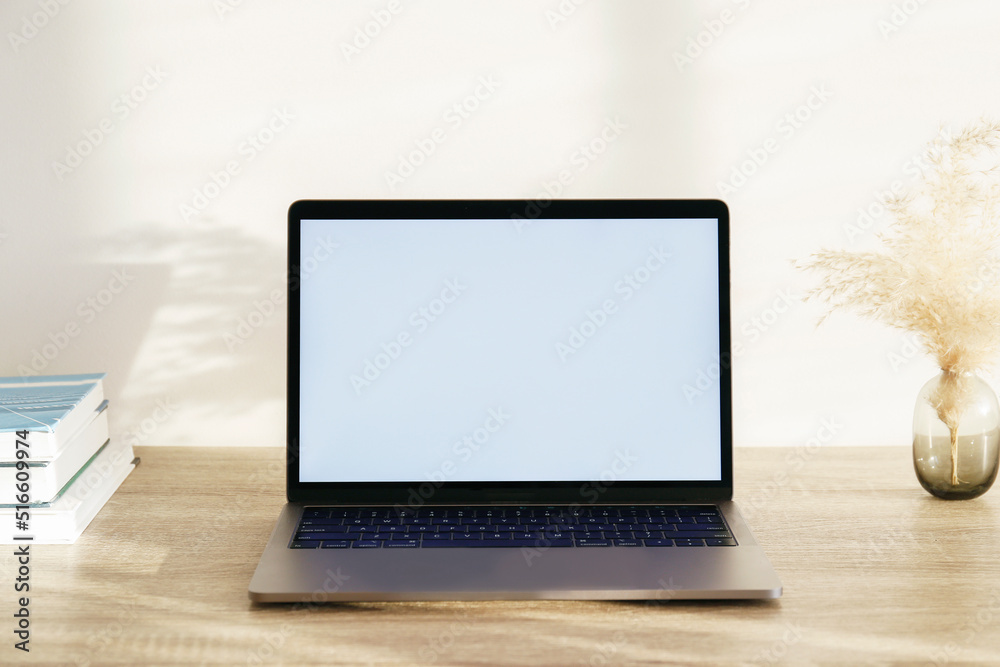 Wall mural Blank screen laptop, cell phone and a stack of books on wooden table. Close up, copy space, white wall background.