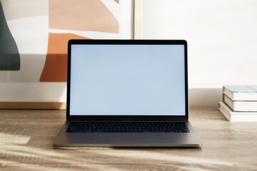 Blank screen laptop, cell phone and a stack of books on wooden table. Close up, copy space, white wall background.