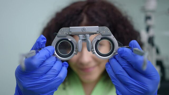 Patient POV of blurred doctor putting on lens frame close-up. Caucasian professional woman with eyesight check tool in ophthalmologic clinic. Optometry and ophthalmology concept