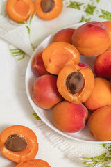 Whole and peeled orange apricots close up in a white plate. Healthy vegan eating concept.