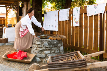 a woman in the national dress of an East European peasant Slavic Russian Ukrainian at a well with a rocker on a rural farmstead is collecting water in a bucket