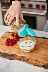 A woman topping yogurt with granola in a bright modern kitchen