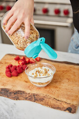 A woman topping yogurt with granola in a bright modern kitchen