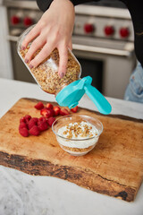 A woman topping yogurt with granola in a bright modern kitchen