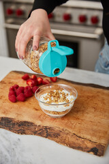A woman topping yogurt with granola in a bright modern kitchen