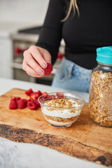 A woman topping yogurt and granola with fruit in a bright modern kitchen