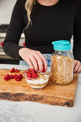 A woman topping yogurt and granola with fruit in a bright modern kitchen