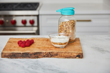 Yogurt with granola, and raspberries and strawberries next to jar with granola in a bright modern kitchen