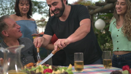 Family barbecue at backyard. Adult son bringing food and serving father during holidays celebration. Father and son bonding moment