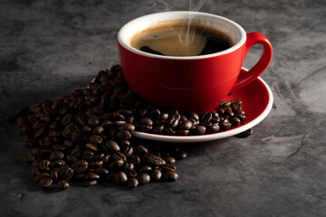 Fototapeta premium Hot espresso in red coffee mug with coffee beans on concrete