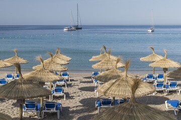 Straw umbrellas and sunbeds on a sandy beach by the sea. In the background the ship, the island. Beautiful sunny day on the Spanish coast, Europe.