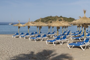 Straw umbrellas and sunbeds on a sandy beach by the sea. In the background the ship, the island....