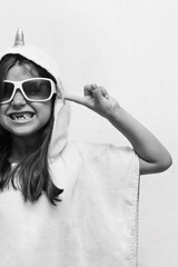 Little crazy happy girl in glasses shows her teeth and closes her ears on a white background,...