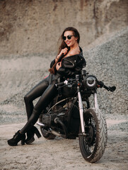 Obraz na płótnie Canvas beautiful girl with long dark hair red lips in a black jacket and black pants sits on a black vintage motorcycle in an industrial zone
