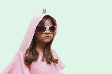 little girl in a pink poncho and sunglasses very serious, funny child in a unicorn costume isolated on a blue background,